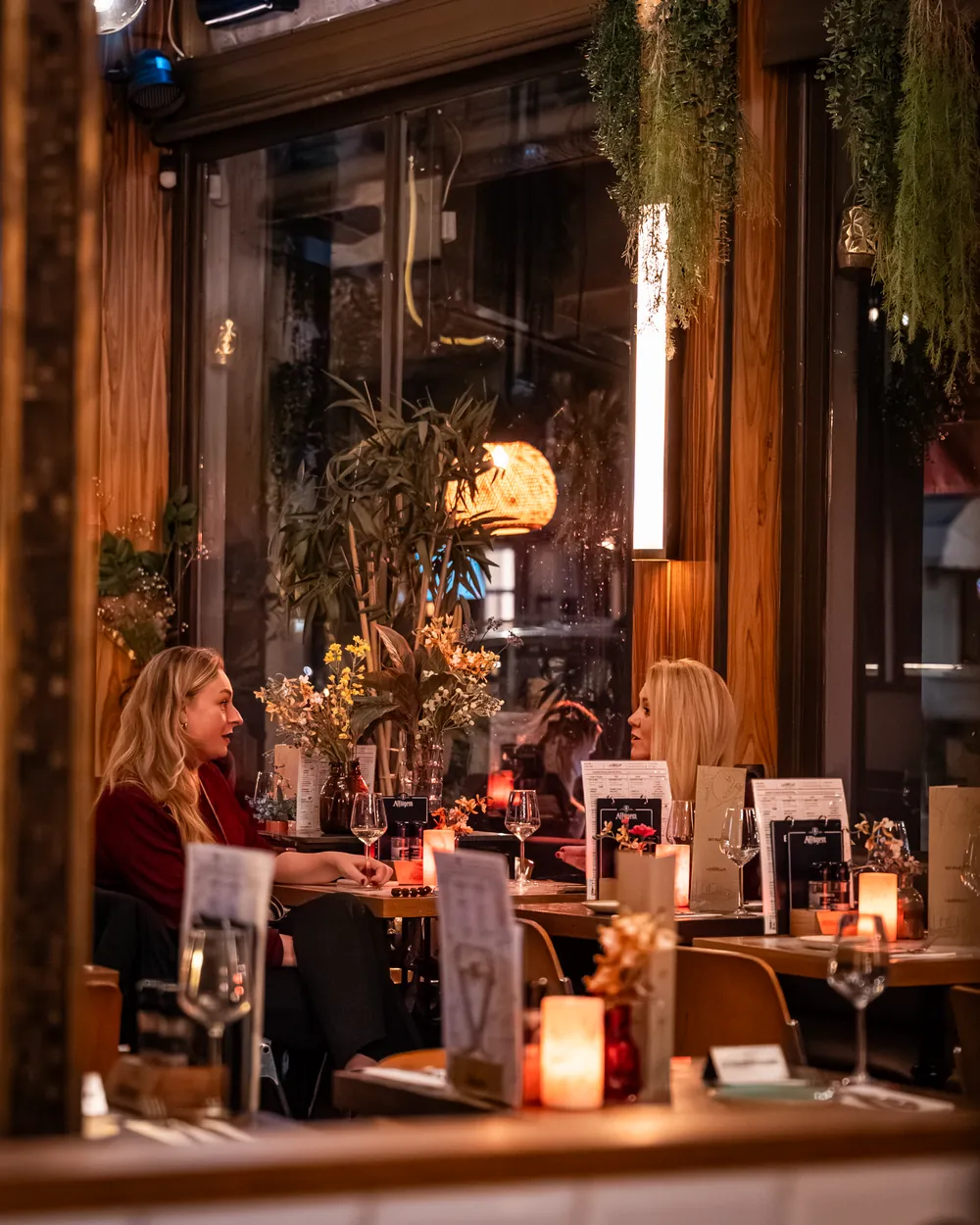 Twee gasten aan een raamtafel bij kaarslicht
